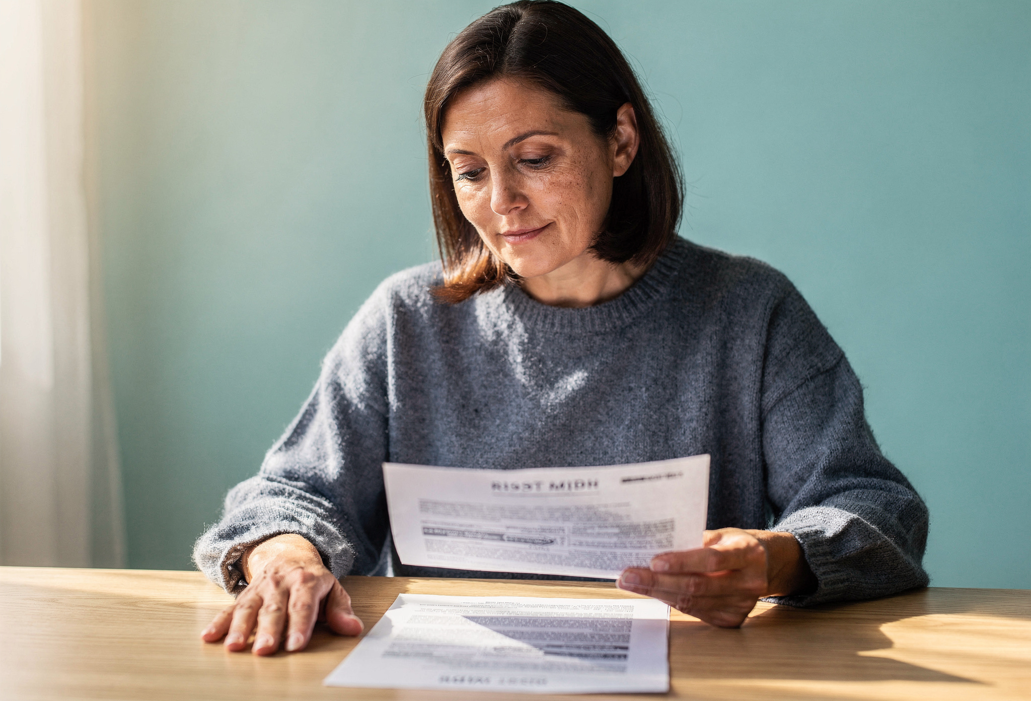Woman in her forties reviewing a printed real-estate document at an oak table