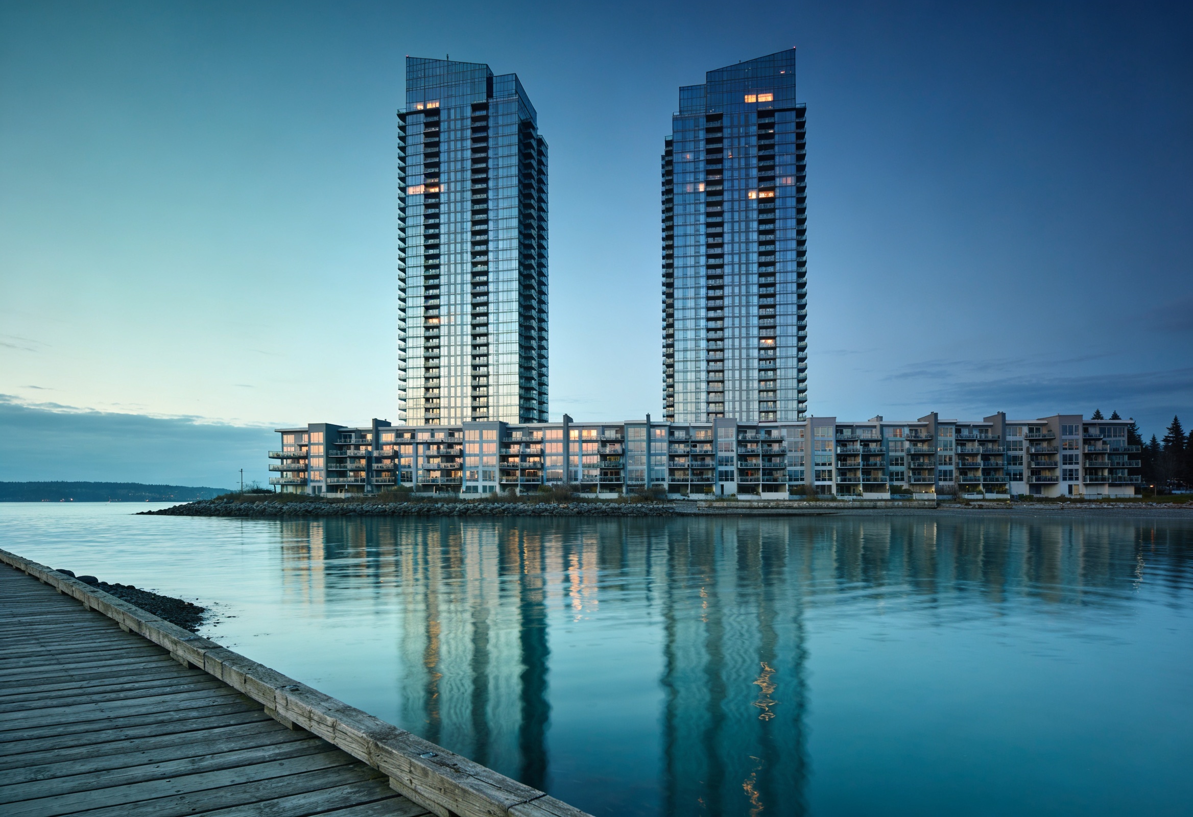 Waterfront condominium towers reflected in a calm harbour inlet at dusk